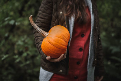 Midsection of woman holding pumpkin while standing against plants