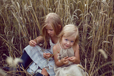 Two blonde sisters sit in a field among dry wheat in the summer