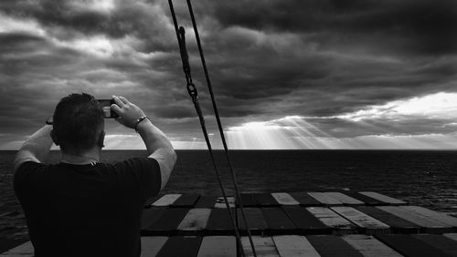Photographer in the frame, rear view of man photographing sea against sky