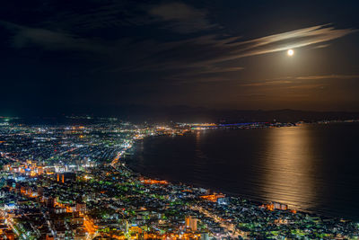 High angle view of illuminated city by sea against sky