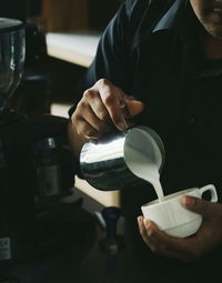 Midsection of barista pouring milk in coffee cup at cafe