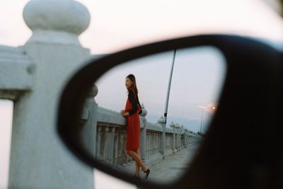 Woman standing by car against sky