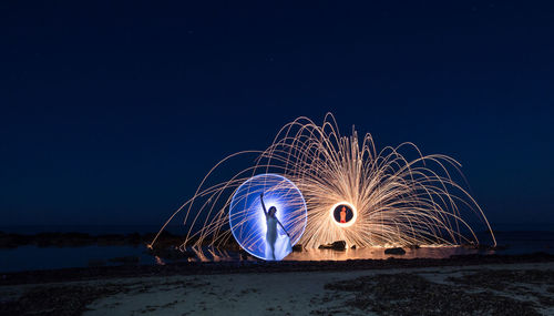 Light trails on beach against clear blue sky at night