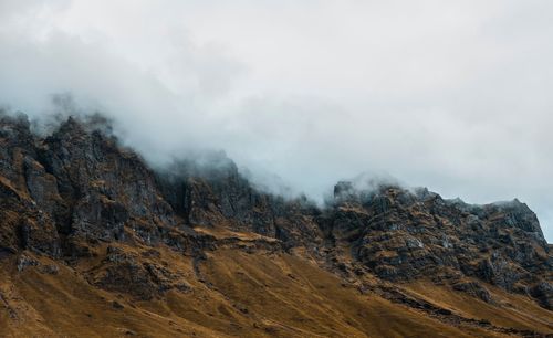 Low angle view of clouds covering rocky cliff in foggy weather