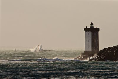 Lighthouse at sea shore against clear sky