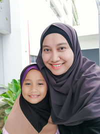 Portrait of smiling mother and daughter wearing hijab in city
