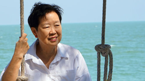 Woman looking away by ropes against sea and sky