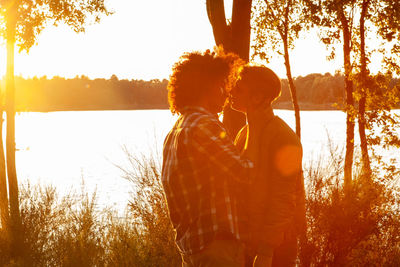 Rear view of woman standing against trees during sunset