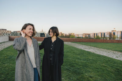 Smiling lesbian couple walking in park against clear sky