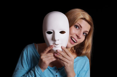 Portrait of young woman holding mask against black background