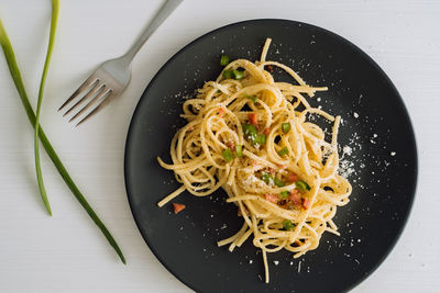 Spaghetti pasta sprinkled with cheese parmesan and green onions on a black plate 