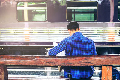 Rear view of man sitting at railroad station platform