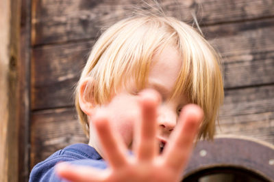 Portrait of boy showing stop gesture while standing against built structure