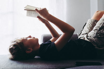 Boy reading book on sofa at home