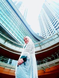 Full length of smiling woman standing against modern buildings in city