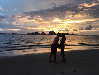 Friends enjoying at beach against sky during sunset