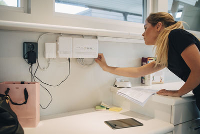 Teenage girl adjusting cable of equipment mounted on wall at home