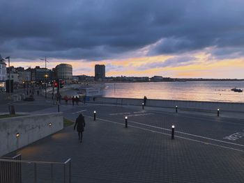 People on railing by sea against sky at sunset