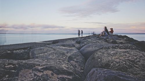 Woman on rock at beach against sky during sunset
