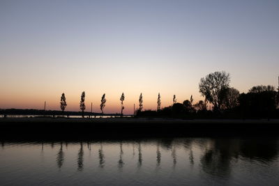 Silhouette trees by lake against clear sky during sunset