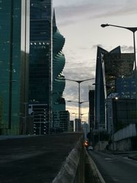 Illuminated street amidst buildings against sky at sunset