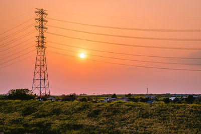 Low angle view of electricity pylon on field against sky during sunset