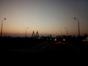 Vehicles on road against sky during sunset