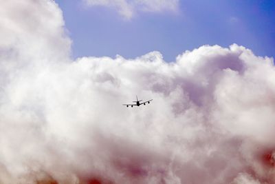 Low angle view of silhouette airplane flying against cloudy sky during sunset