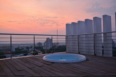 Swimming pool in city against sky during sunset