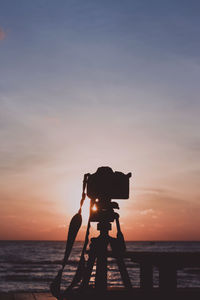 Silhouette camera on beach against sky during sunset