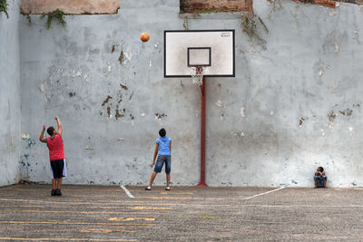 Rear view of people playing basketball against wall