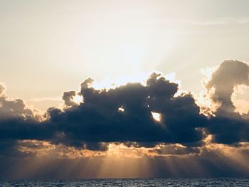 Sunlight streaming through clouds over sea during sunset