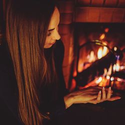 Woman with long hair sitting by fireplace at home