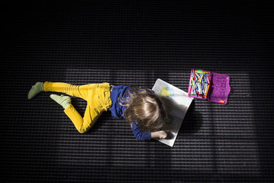 High angle view of girl drawing on book while lying on bed