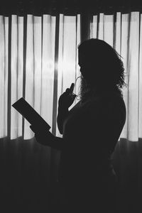 Side view of silhouette woman holing book standing at home