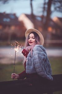 Side view of young woman holding sparkler while standing at park