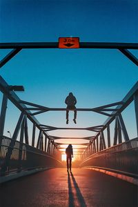 Silhouette men on footbridge against sky during sunset