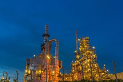 Low angle view of illuminated factory against blue sky