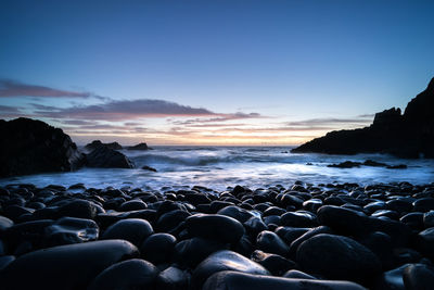 Rocks on beach against sky during sunset