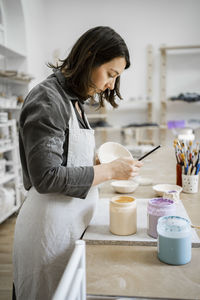 Young craftswoman painting on bowl in workshop