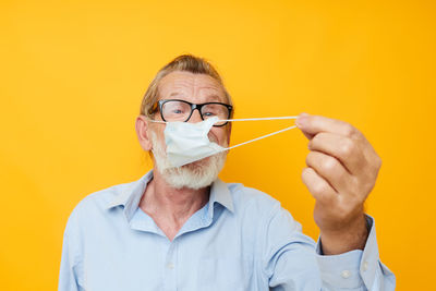 Portrait of senior man wearing mask against yellow background