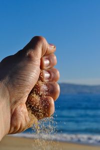 Close-up of hand against sea against clear blue sky