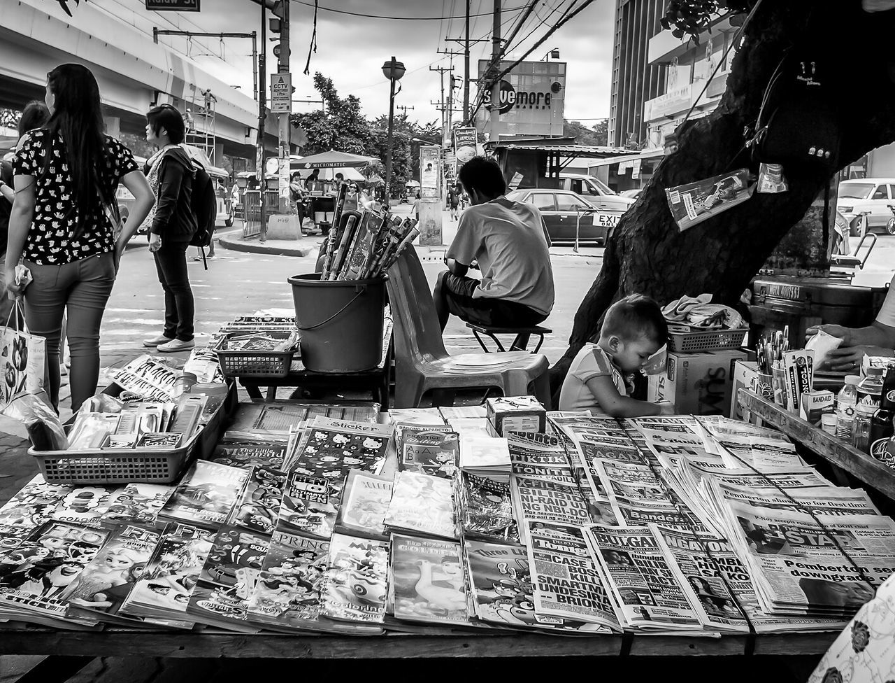 person, men, lifestyles, large group of people, retail, market, leisure activity, market stall, for sale, architecture, shopping, built structure, indoors, sitting, casual clothing, city life, medium group of people, food and drink, building exterior