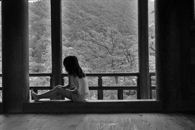 Full length of woman relaxing on window against trees