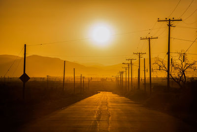 Silhouette electricity pylons against sky during sunset
