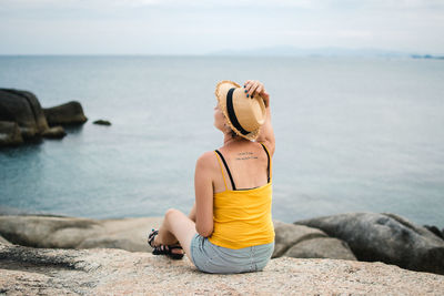 Young woman sitting on rock by sea against sky