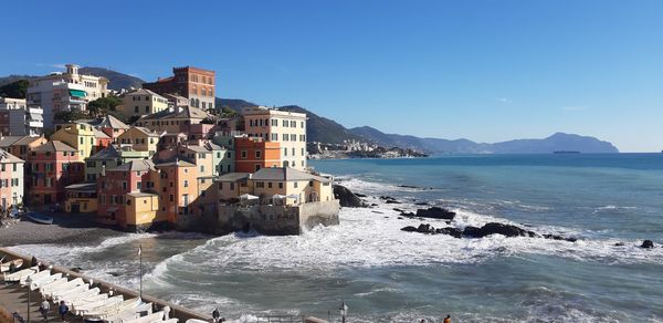 Buildings by sea against clear blue sky