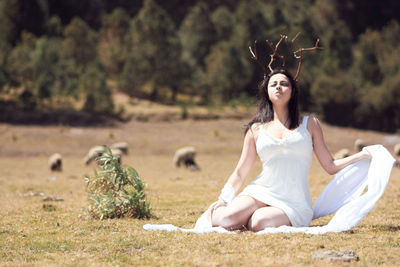 Beautiful woman wearing artificial horn while sitting on field
