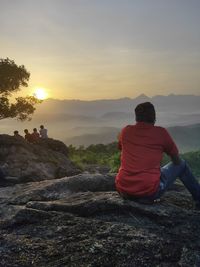 Rear view of man sitting on rock at sunset