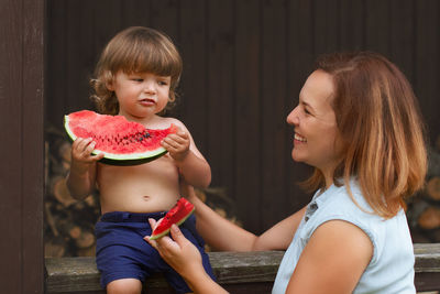 Smiling mother feeding watermelon to son outdoors